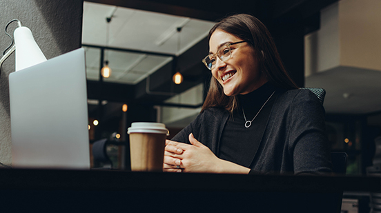 A businesswoman smiling, sitting in front of a laptop and coffee cup